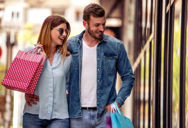 Sokakta alışveriş yapan genç bir çift ellerinde alışveriş torbalarıyla eğleniyor..