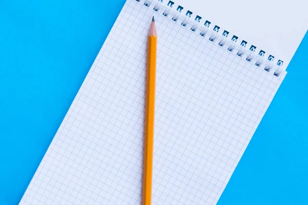 Partial view of an opened caged notebook with pencil over turquoise background. Flat view. Copy space. Business and school concept
