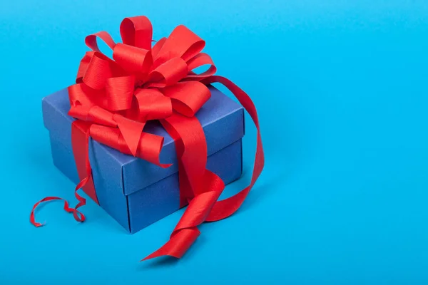 Голубая подарочная коробка с красной лентой и бантом на синем фоне — стоковое фото
