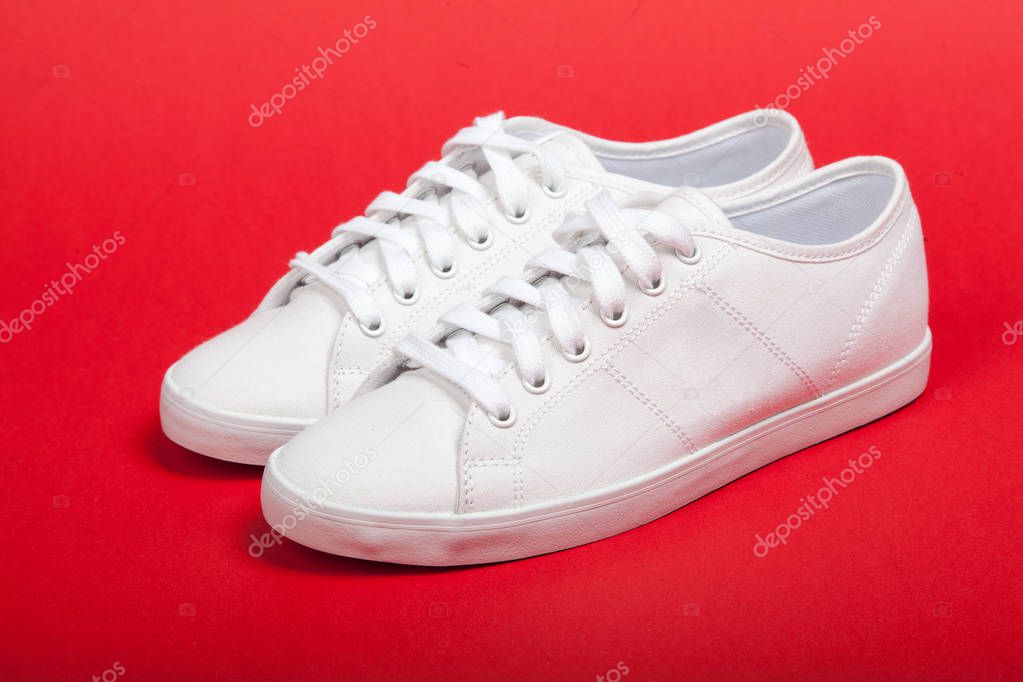 Pair of new white sneakers on red background
