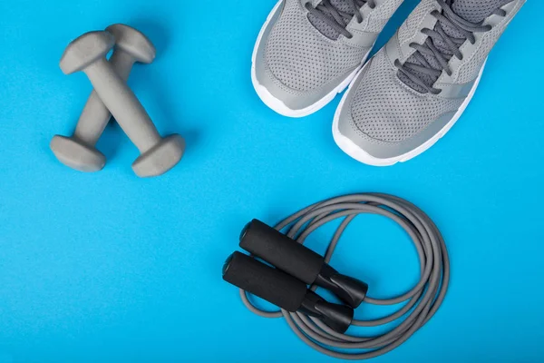 Sport shoes, dumbbells and skipping rope on blue background. Top view. Fitness, sport and healthy lifestyle concept.