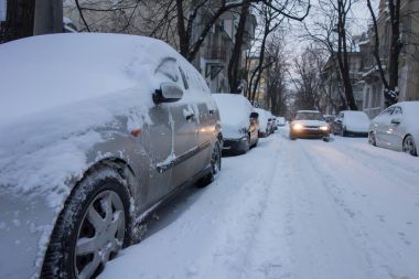 Urban street after snow storm. Cars covered with snow clipart