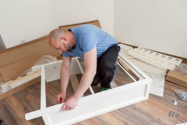 Yeni evde sıradan giyinmiş mobilya montajı yapan bir adam. Marangoz evde mobilya onarıp monte ediyor.