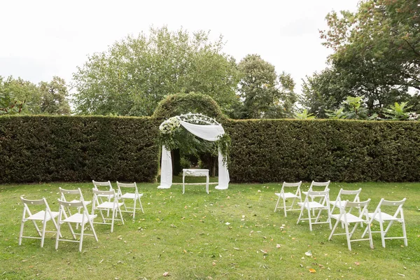 Hochzeitszeremonie. Hochzeitsbogen und weiße Stühle auf grünem Rasen im Garten. — Stockfoto