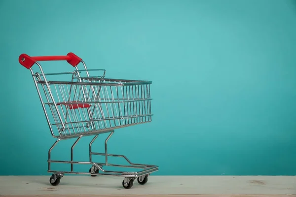 Prázdný nákupní vozík na dřevěný stůl s zeleným pozadím. Koncept konzumu. Online nakupování koncept. — Stock fotografie