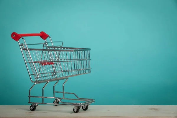 Carrito de compras vacío en mesa de madera con fondo verde. Concepto de consumismo. Concepto de compras online . — Foto de Stock