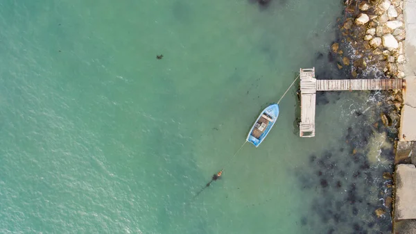 Одинокая рыбацкая лодка и деревянный пир в бирюзовом океане, море. Фото с воздуха, вид сверху — стоковое фото