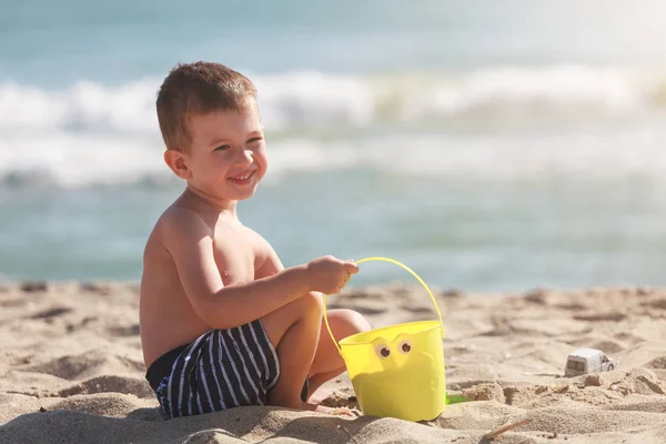 Mały szczęśliwy chłopiec bawić się piaskiem i zabawkami na letniej plaży — Zdjęcie stockowe