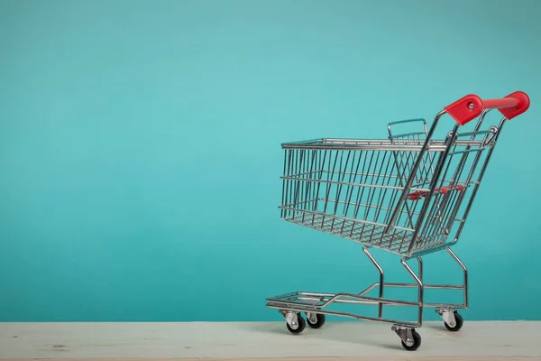 Carrito de compras vacío en mesa de madera con fondo verde. Concepto de consumismo. Concepto de compras online . — Foto de Stock