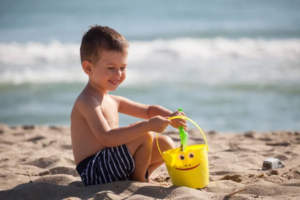 Mały szczęśliwy chłopiec bawić się piaskiem i zabawkami na letniej plaży — Zdjęcie stockowe
