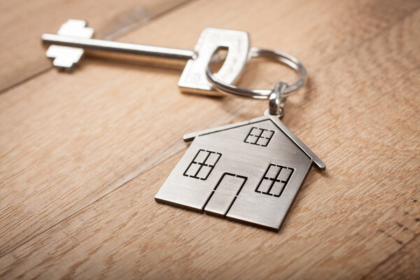 Close up silver home shaped keychain with key on wooden background. Mortgage, investment, real estate, property and new home concept