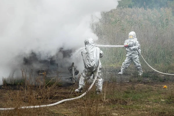 Dois bombeiros de fato de protecção trabalham com mangueira de água. Lutando por um ataque de fogo — Fotografia de Stock