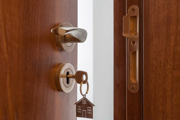 Ανοιχτή πόρτα σε ένα νέο σπίτι. Λαβή πόρτας με μπρελόκ σε σχήμα κλειδιού και σπιτιού. Υποθήκη, επένδυση, ακίνητη περιουσία, ακίνητα και νέα έννοια της κατοικίας — Φωτογραφία Αρχείου
