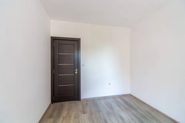 Gesloten houten deur in lege kamer, houten vloer. Witte muren — Stockfoto