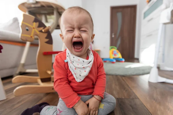 Kislány, aki otthon ül a földön és sír. Egy éves baba sír. — Stock Fotó