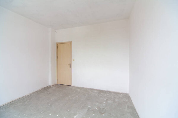 Закрытая деревянная дверь в пустой комнате, белые стены. Новая пустая комната в стадии строительства. Реконструкция интерьера. 