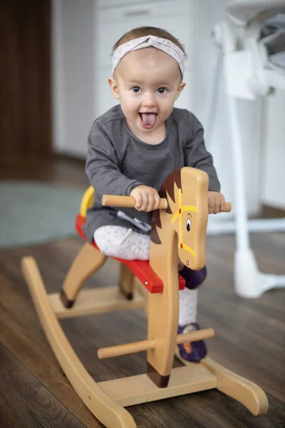 Menina bebê feliz jogando no cavalo de balanço de madeira. Infância, jogo em casa conceito — Fotografia de Stock
