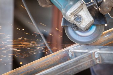 Metal kesen elektrikli öğütücü kullanan bir fabrika işçisi. Parıltılar