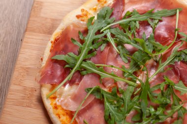 Tahta üzerinde jambonlu, peynirli ve roka olan pizza.