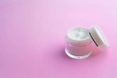 Pembe arka planda açık kapaklı krema kavanozu. 