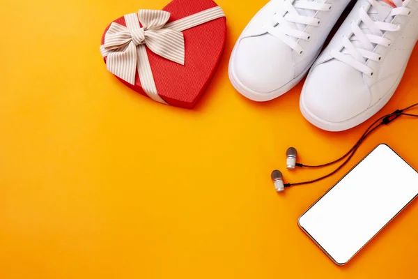 Telefon düzeni, spor ayakkabıları, kulaklıklar ve yaylı kırmızı kalp.