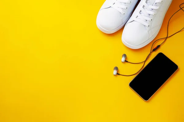 Sarı arka planda spor ayakkabıları, telefon ve kulaklıklar.