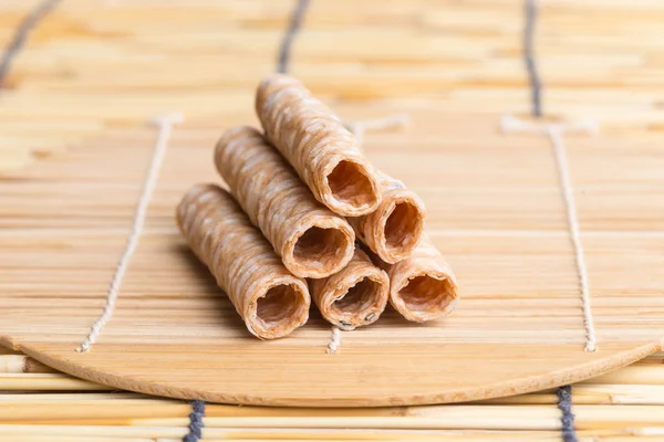 Crispy rolled wafer sticks, traditional dessert in Thailand, are collocated on the wood board.