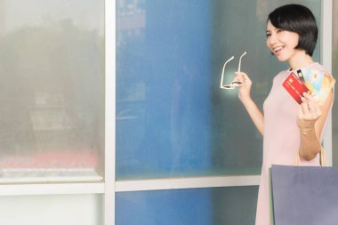 Pembe elbiseli, alışveriş çantası taşıyan ve kredi kartı gösteren Asyalı güzel bir kız.