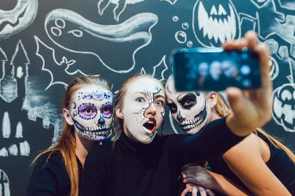 Três meninas que vão no Halloween, grimace fazer selfie um fundo escuro com padrão — Fotografia de Stock