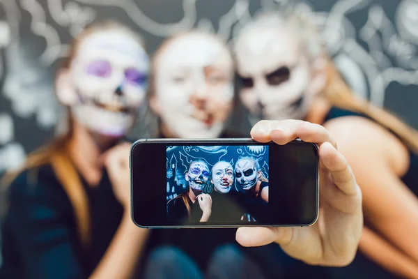 Tres chicas van en Halloween, mueca hacer selfie un fondo oscuro con patrón —  Fotos de Stock