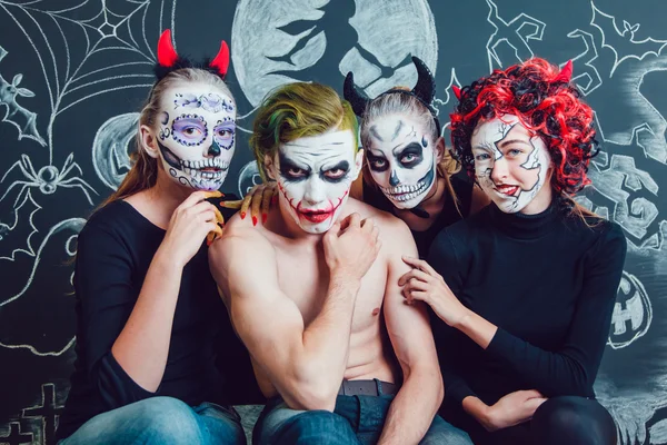 Три девушки и парень с рисунком лица Хэллоуина на темном фоне — стоковое фото
