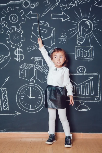 Маленька дівчинка показує вказівник на стіну з діловим або шкільним зображенням — стокове фото