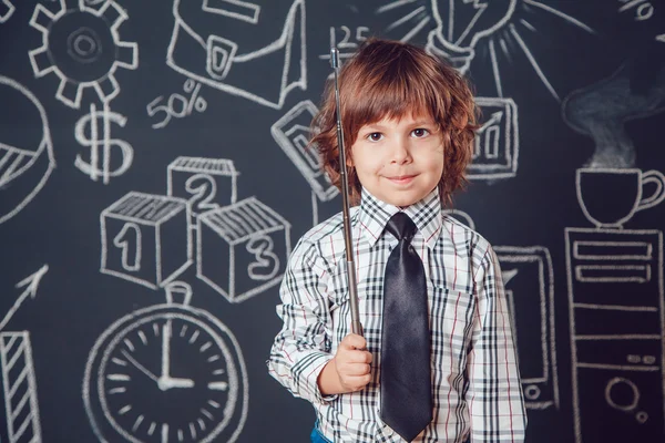 Mały chłopiec jako biznesmen lub nauczyciel stojący i trzymając wskaźnik na ciemnym tle z obrazem szkoły biznesu — Zdjęcie stockowe