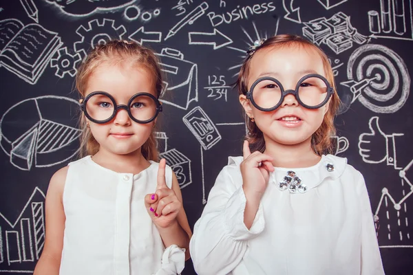 两个戴着眼镜的小女孩举起手指在墙上，墙上有商业或学校的照片 — 图库照片