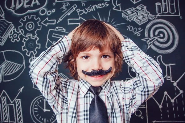 Little boy as businessman or teacher with mustache standing on dark background pattern. Wearing shirt and tie. He keeps holding his head. close-up