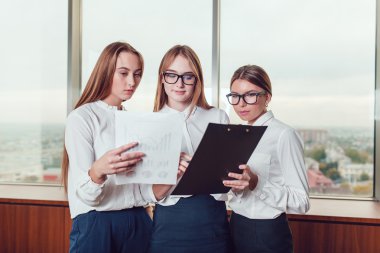 Üç iş kadınları pencere karşı ayakta ve belgeleri çalışma