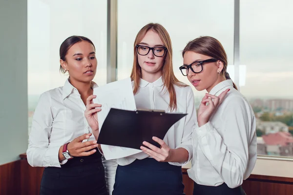 Een Aziatische en twee Europese zakelijke vrouwen permanent tegen het raam bestuderen de documenten — Stockfoto