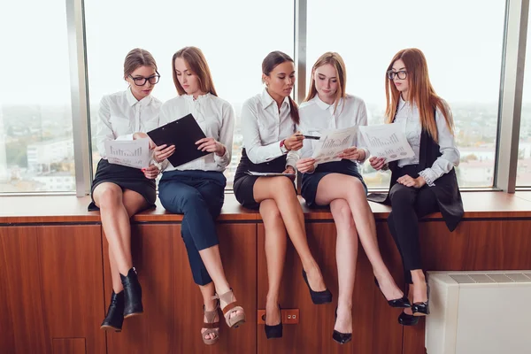 Vijf zakelijke vrouwen zitten op de vensterbank praten en bestuderen van documenten — Stockfoto