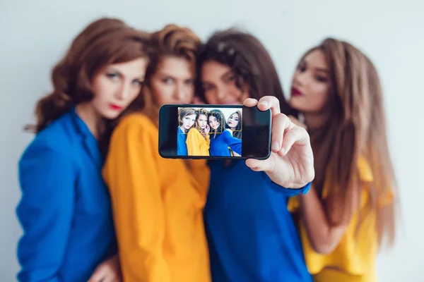 Fashion girls in bright clothes make selfie. Beautiful women with professional makeup and crazy hair style, over white background. — Stock fotografie