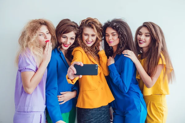 Fashion girls in bright clothes make selfie. Beautiful women with professional makeup and crazy hair style, over white background. — ストック写真