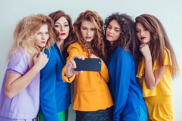 Fashion girls in bright clothes make selfie. Beautiful women with professional makeup and crazy hair style, over white background. — Stock fotografie