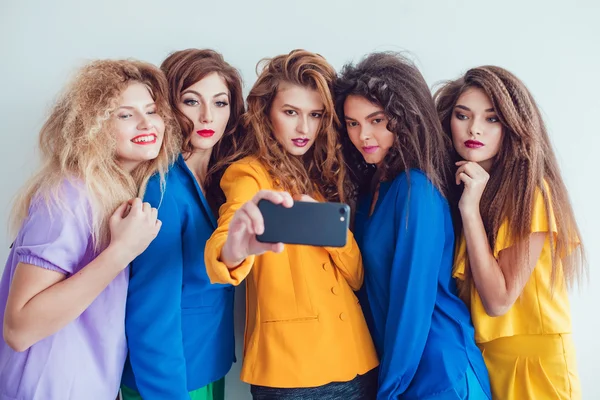 Fashion girls in bright clothes make selfie. Beautiful women with professional makeup and crazy hair style, over white background. — Stock fotografie