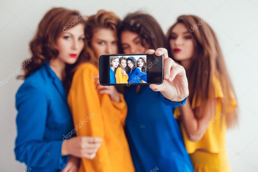 Fashion girls in bright clothes make selfie. Beautiful women with professional makeup and crazy hair style, over white background.