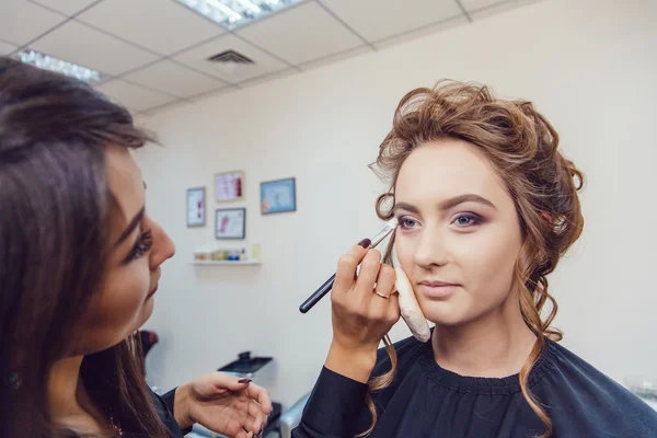 Maskör gör professionell makeup av ung kvinna i skönhetsstudio — Stockfoto