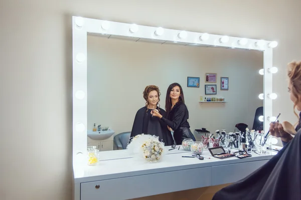 Make-up artiest doen professionele make-up van jonge vrouw in de spiegel kijken — Stockfoto