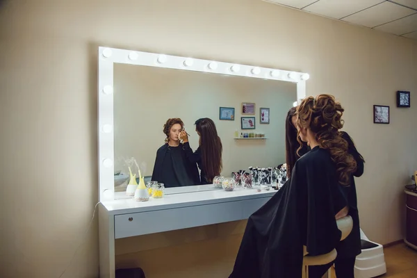 Kunstenaar doen professionele make-up van jonge vrouw in de buurt van de spiegel in schoonheid studio make-up — Stockfoto