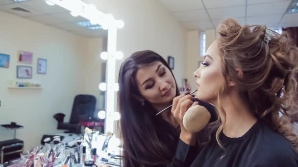Kunstenaar doen professionele make-up van jonge vrouw in de buurt van de spiegel in schoonheid studio make-up — Stockvideo