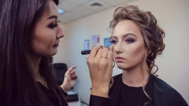 Maskér dělá profesionální make-up mladé ženy v studio krásy