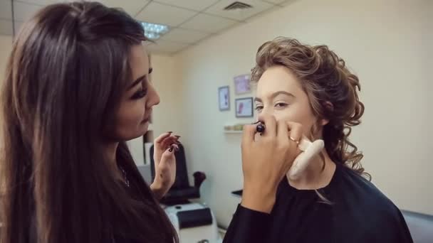 Maskér dělá profesionální make-up mladé ženy v studio krásy — Stock video