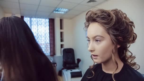 Maskér dělá profesionální make-up mladé ženy v studio krásy — Stock video